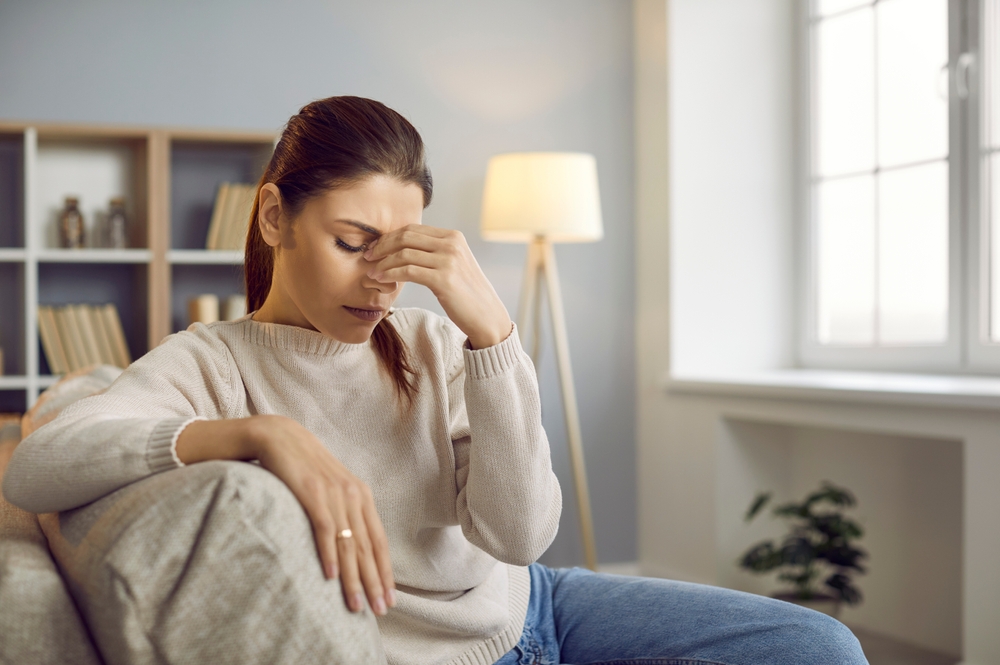 Woman sitting on couch with migraine.